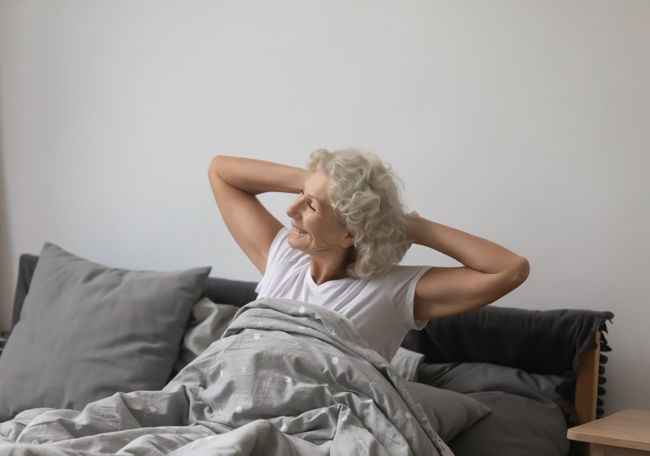An elderly woman stretching in her bed