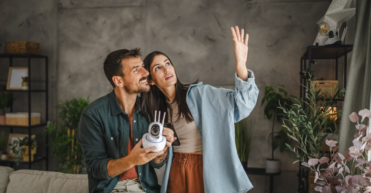 Man holding a smart camera with a woman standing next to him, both looking at their window