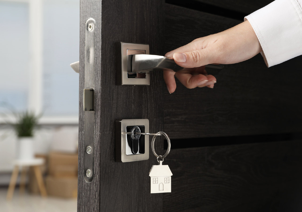 Hand on a door handle closing the door with a key in the lock with a house shaped keychain
