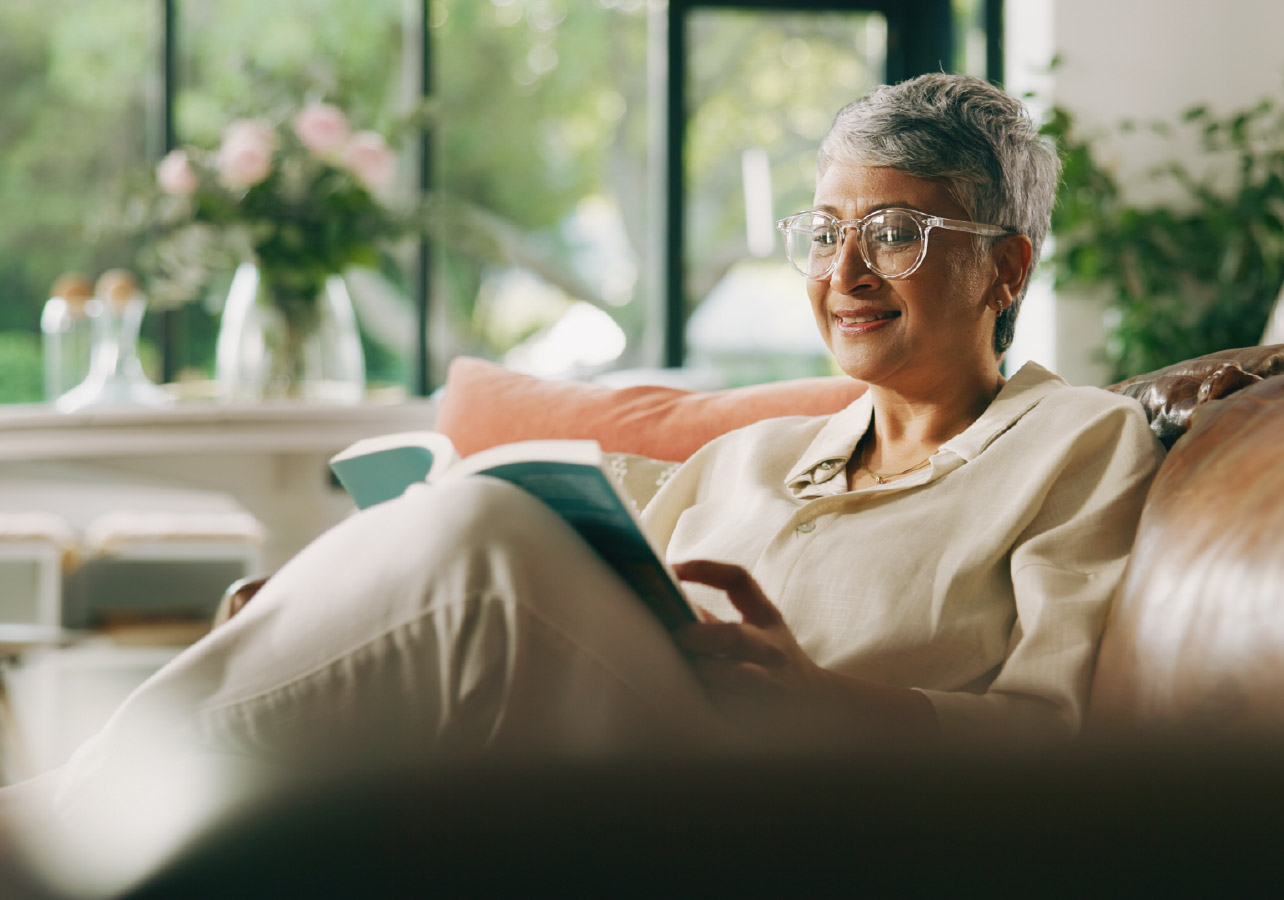 Elderly woman sitting on a couch and reading a book