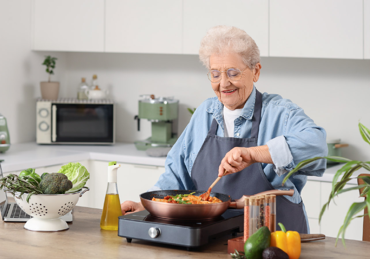 Elderly woman in the kitchen cooking on a hot plate
